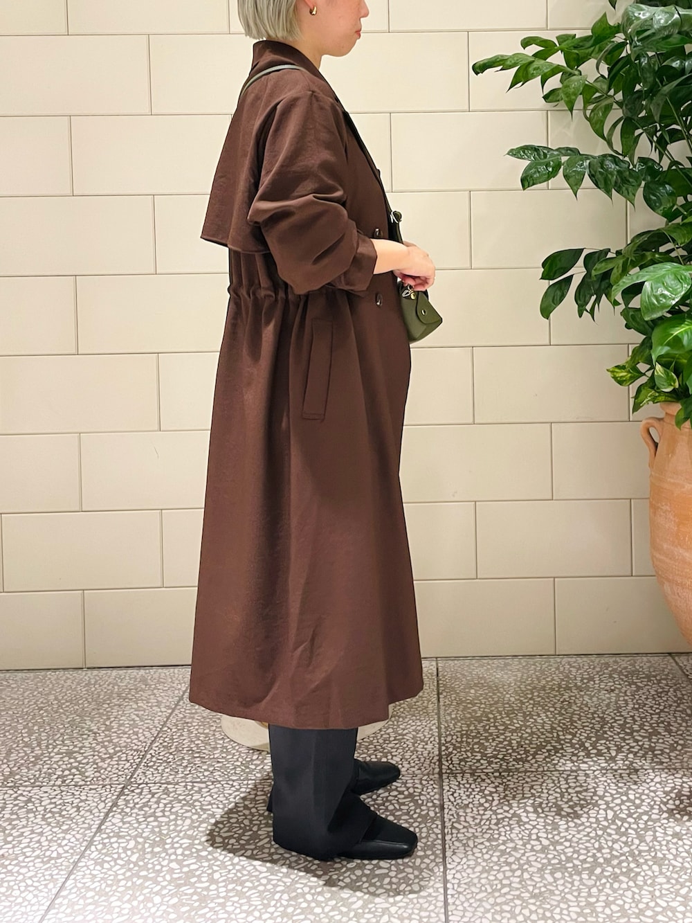 ブラウン系のトレンチコート、ホワイト系のシャツ/ブラウス、グリーン系のショルダーバッグを着用したレディースの秋コーディネートの2枚目の写真