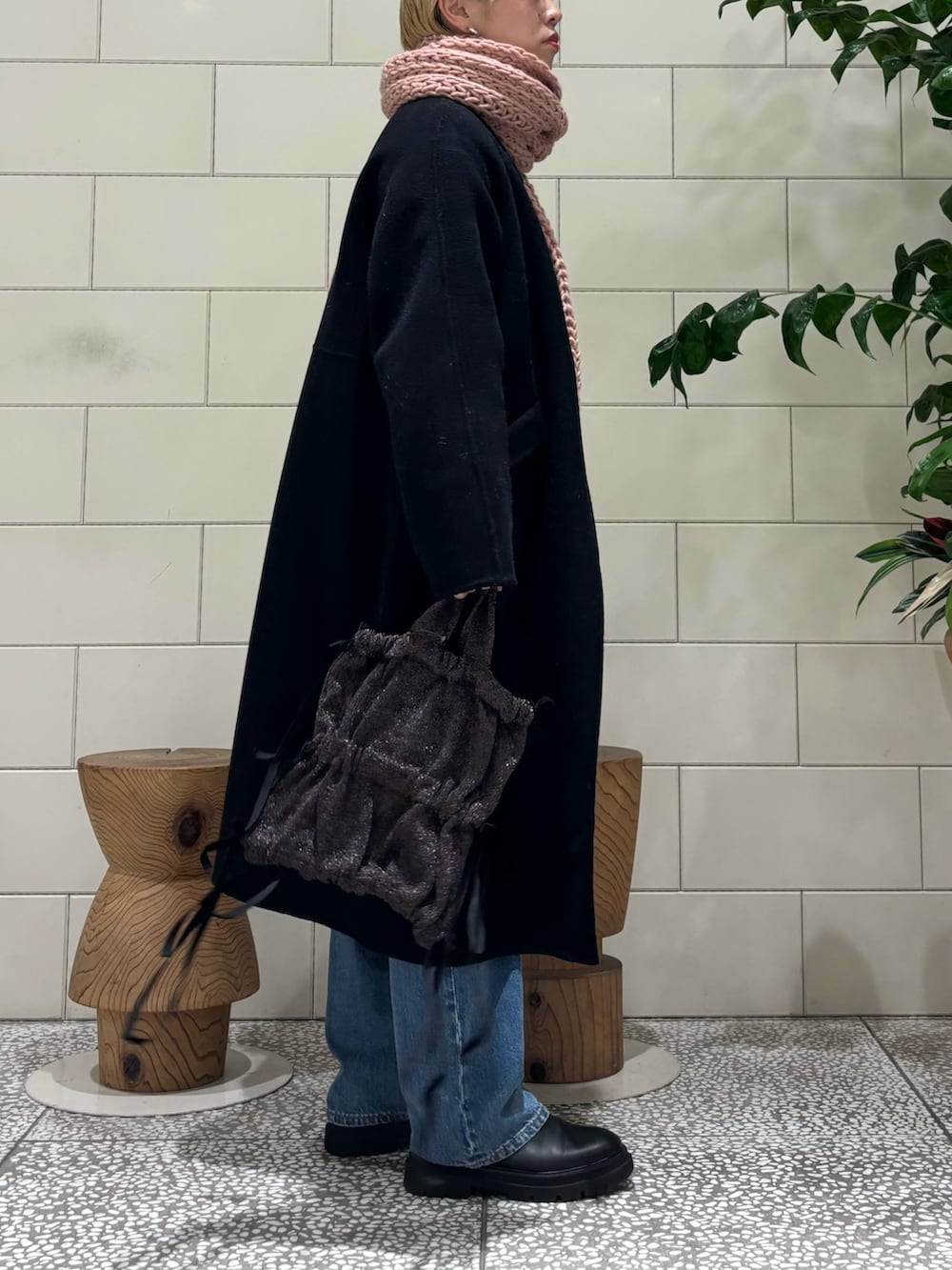 ブラック系のステンカラーコート、グレー系のニット/セーター、ブルー系のデニムパンツを着用したレディースの秋コーディネートの2枚目の写真