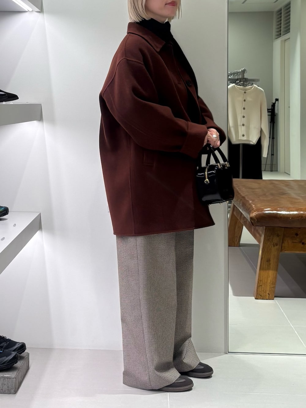 ブラウン系のステンカラーコート、ブラック系のカーディガン/ボレロ、ブラック系のショルダーバッグを着用したレディースの秋コーディネートの2枚目の写真