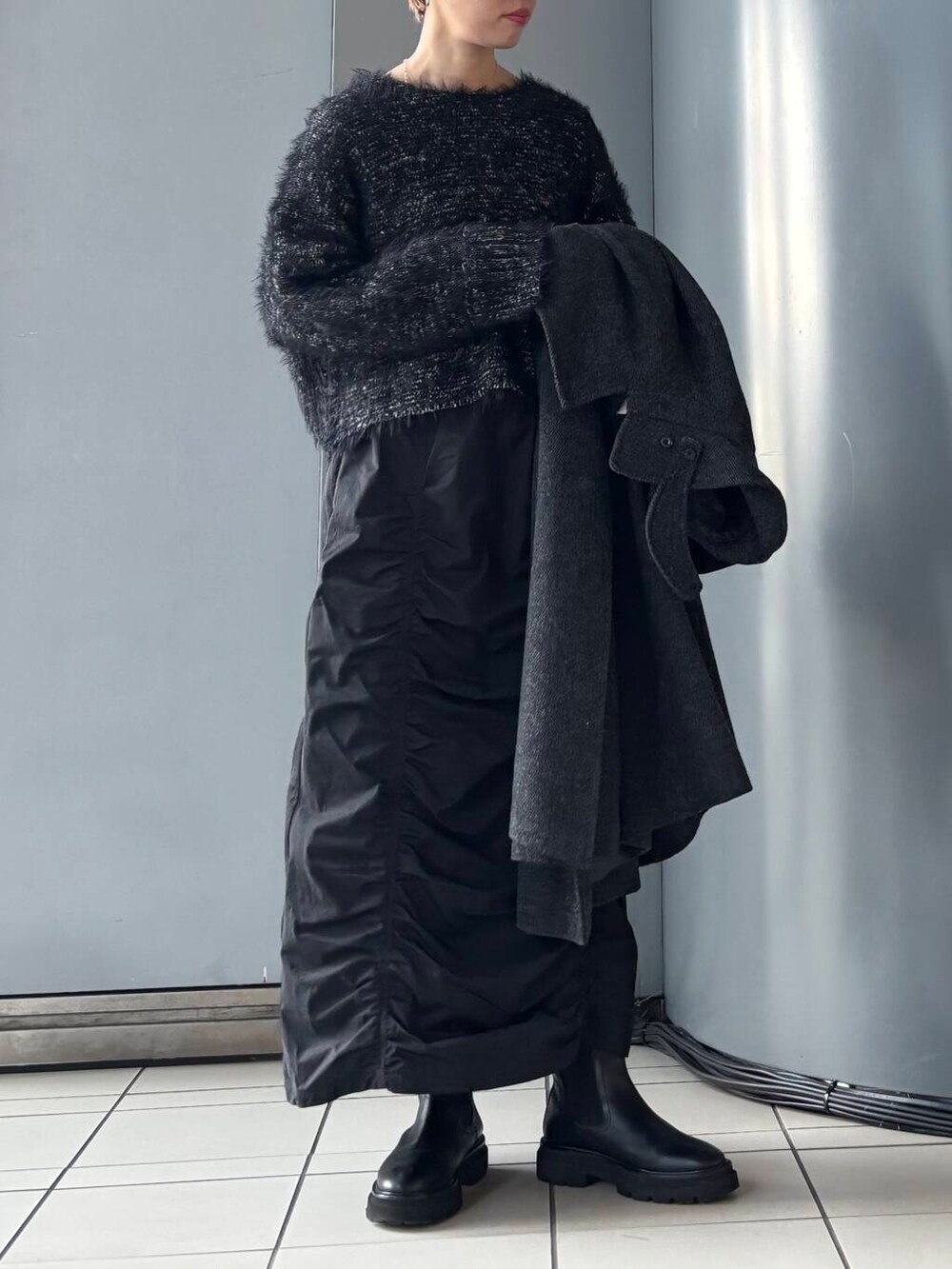 ブラック系のステンカラーコート、ブラック系のスカート、ブラック系のニット/セーターを着用したレディースの冬コーディネートの4枚目の写真