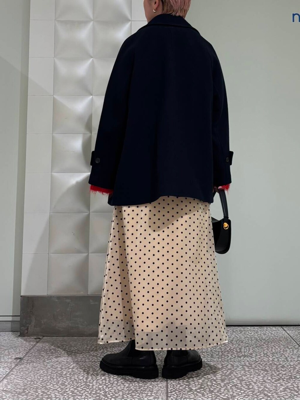 ブルー系のピーコート、レッド系のカーディガン/ボレロ、ベージュ系のスカートを着用したレディースの冬コーディネートの3枚目の写真