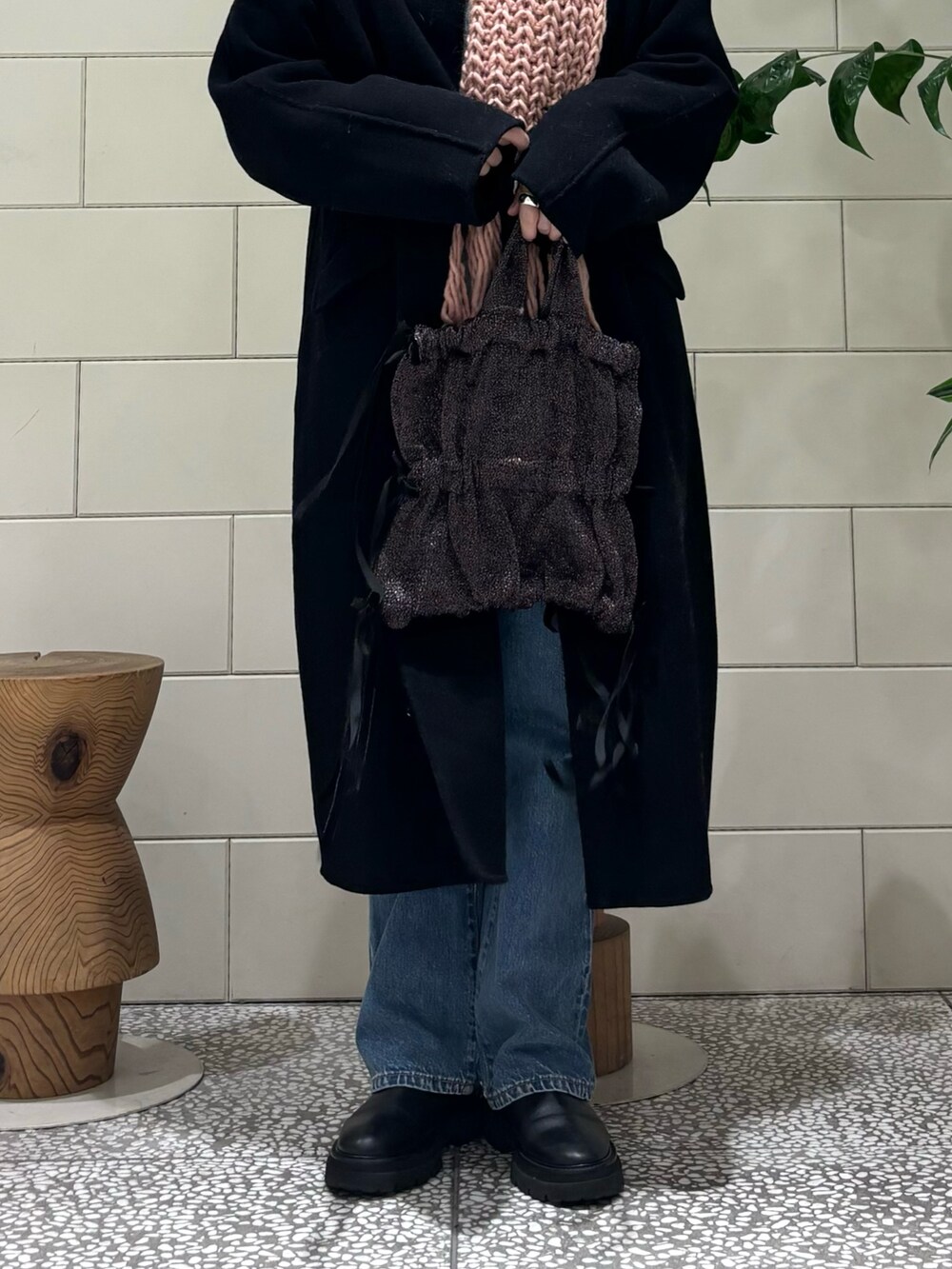 ブラック系のステンカラーコート、グレー系のニット/セーター、ブルー系のデニムパンツを着用したレディースの秋コーディネートの3枚目の写真