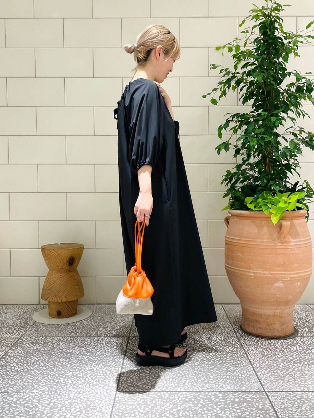 ブラック系のワンピース、ブラック系のサンダル、オレンジ系のハンドバッグを着用したレディースの夏コーディネートの2枚目の写真