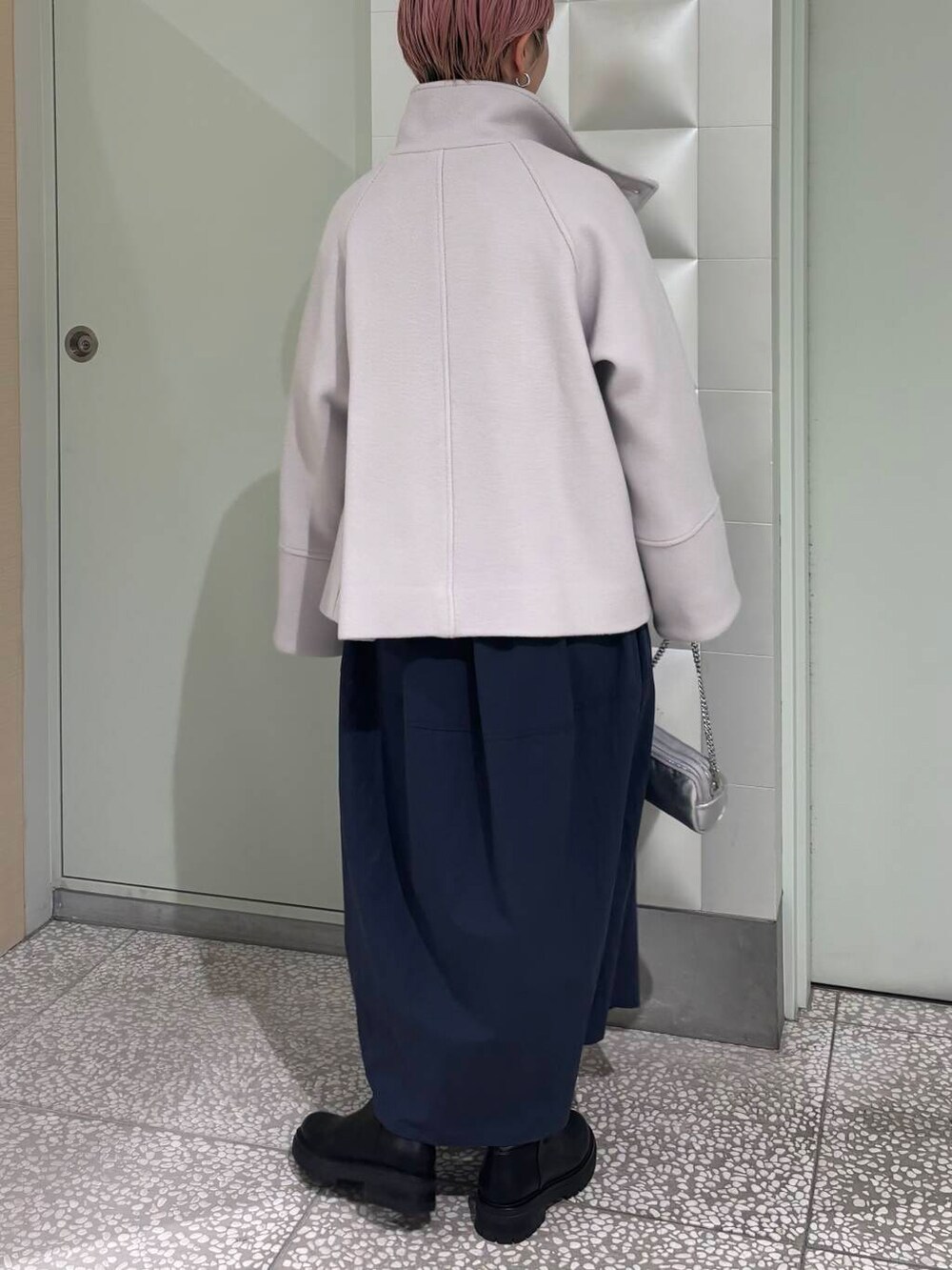 グレー系のピーコート、ブラック系のブーツ、シルバー系のショルダーバッグを着用したレディースの冬コーディネートの3枚目の写真