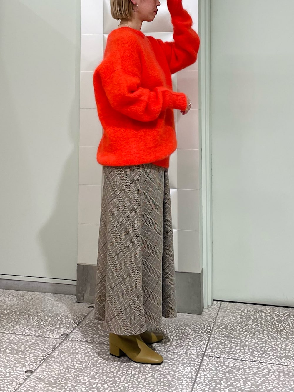 オレンジ系のニット/セーター、ベージュ系のスカート、ベージュ系のブーツを着用したレディースの秋コーディネートの2枚目の写真