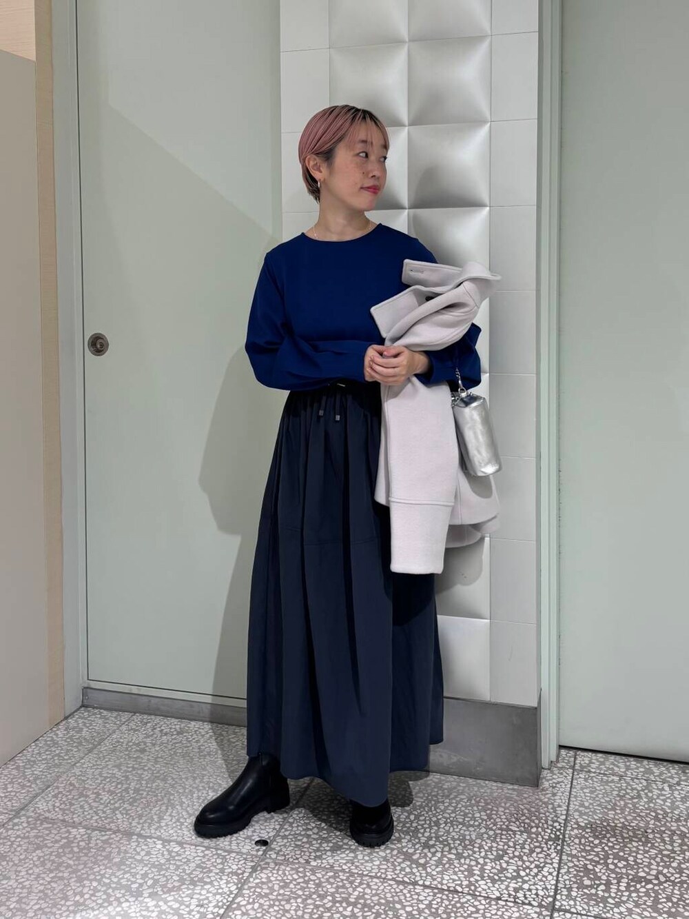 グレー系のピーコート、ブラック系のブーツ、シルバー系のショルダーバッグを着用したレディースの冬コーディネートの4枚目の写真