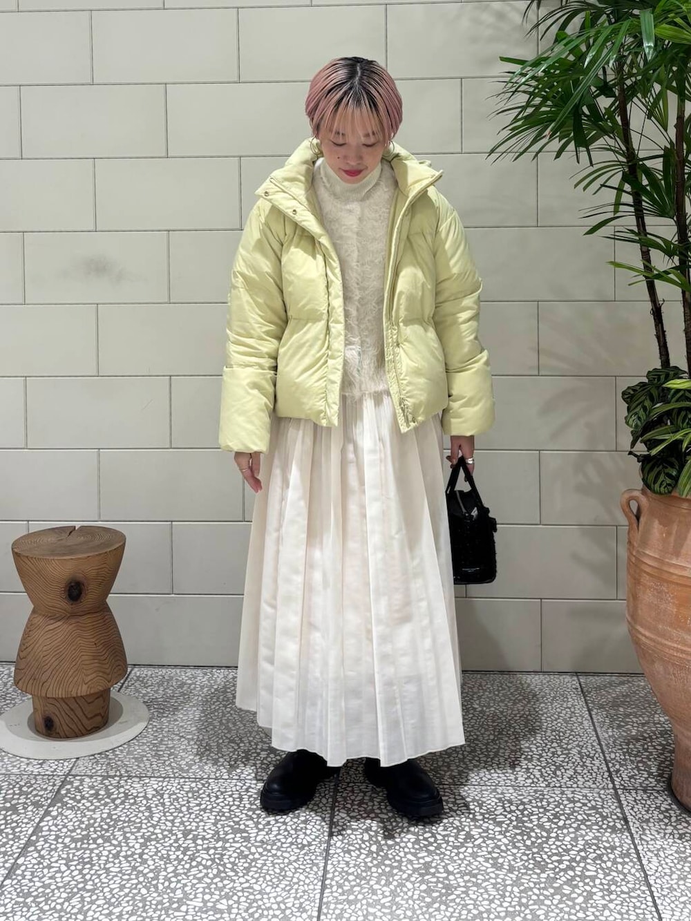 ホワイト系のニット/セーター、ホワイト系のスカート、イエロー系のダウンジャケット/コートを着用したレディースの冬コーディネートの2枚目の写真