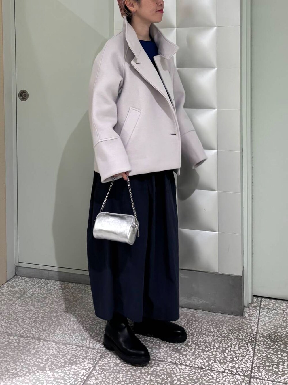 グレー系のピーコート、ブラック系のブーツ、シルバー系のショルダーバッグを着用したレディースの冬コーディネートの2枚目の写真