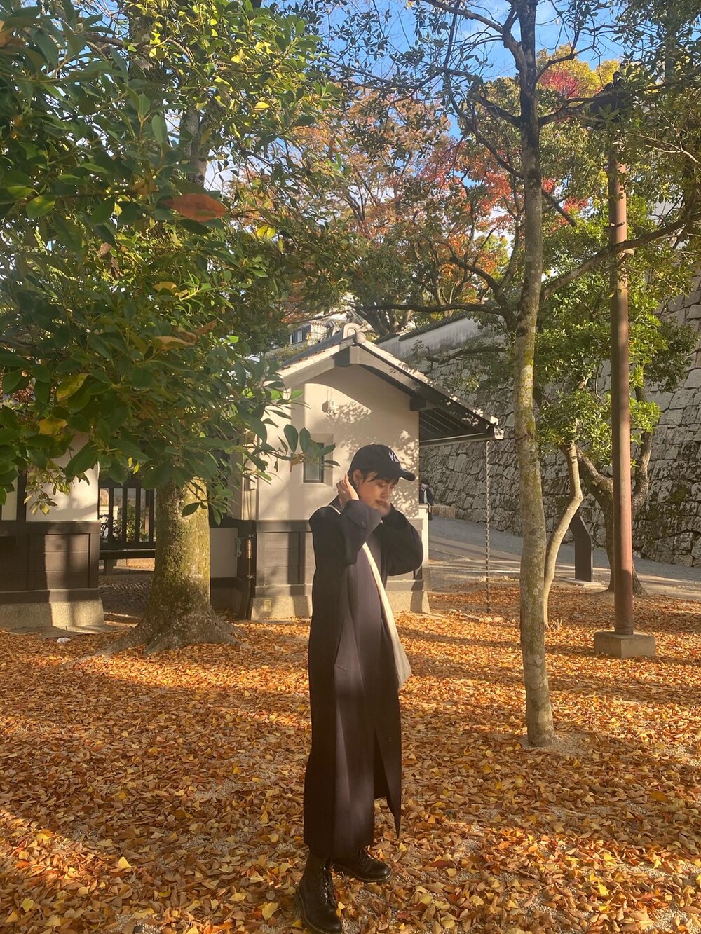 ブラック系のデニムスカート、ホワイト系のショルダーバッグ、ブラック系のブーツを着用したレディースの秋コーディネートの2枚目の写真