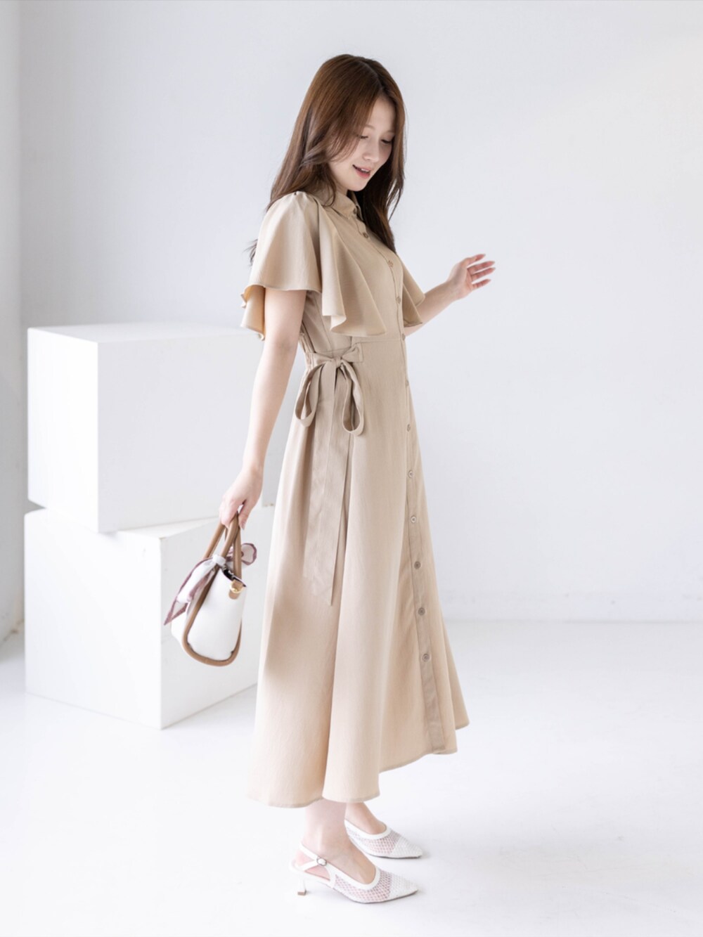 ホワイト系のパンプス、ベージュ系のワンピース、ベージュ系のハンドバッグを着用したレディースの夏コーディネートの3枚目の写真