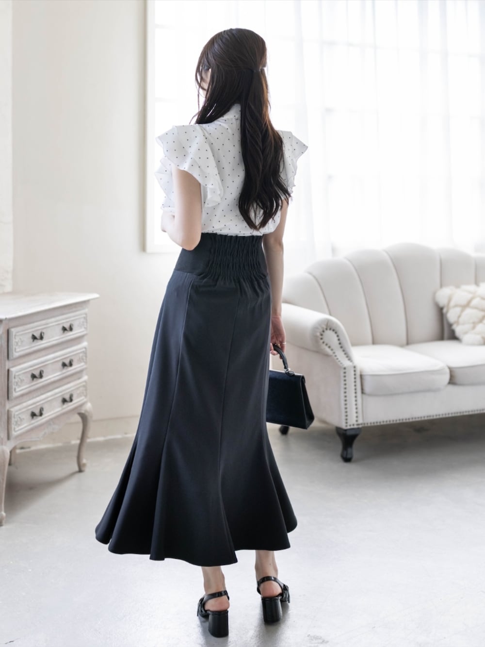 ブラック系のパンプス、ブラック系のスカート、ブラック系のハンドバッグを着用したレディースの夏コーディネートの3枚目の写真