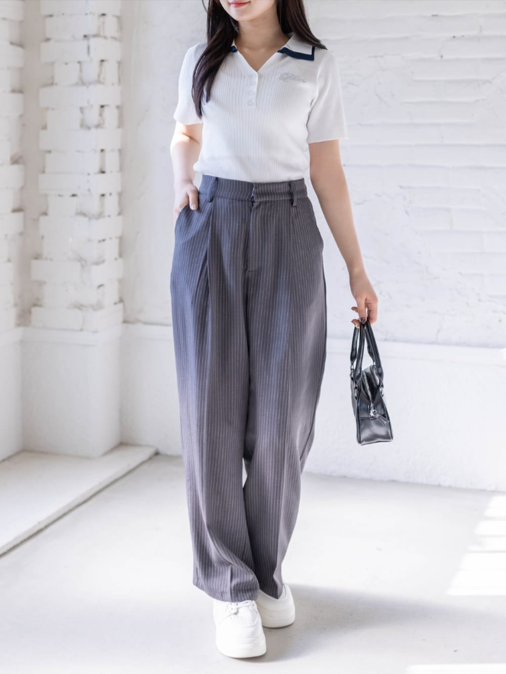 ホワイト系のスニーカー、ブラック系のハンドバッグ、グレー系のスラックスを着用したレディースの春コーディネートの2枚目の写真