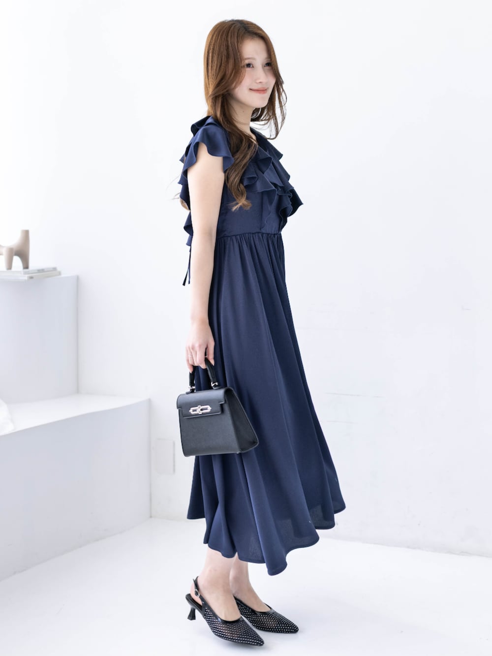 ブラック系のハンドバッグ、ブラック系のパンプス、ブルー系のワンピースを着用したレディースの春コーディネートの2枚目の写真