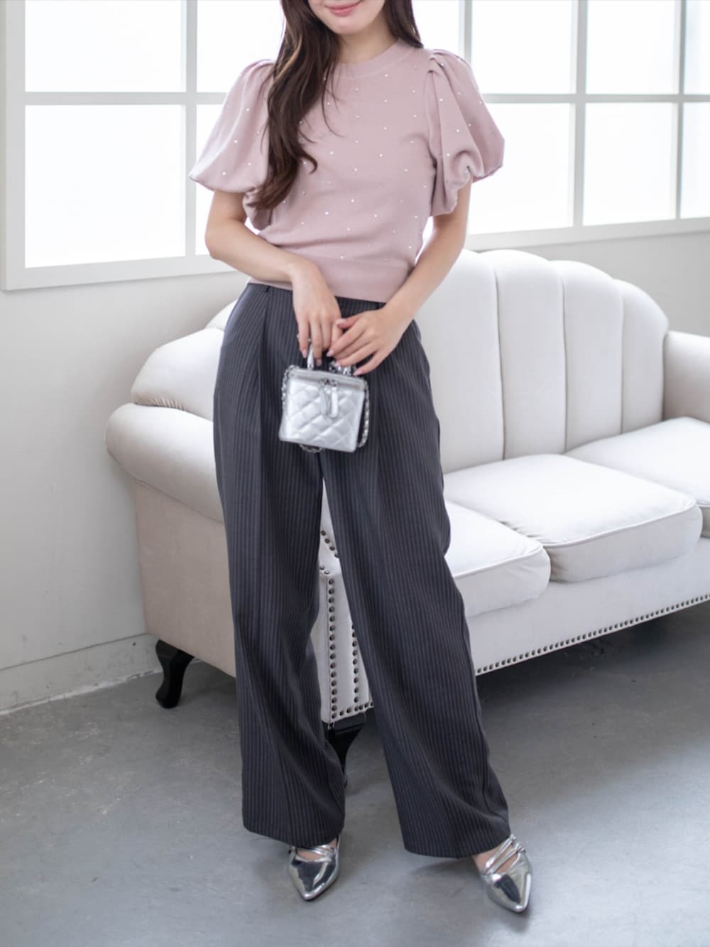 シルバー系のパンプス、グレー系のスラックス、ピンク系のニット/セーターを着用したレディースの夏コーディネートの2枚目の写真