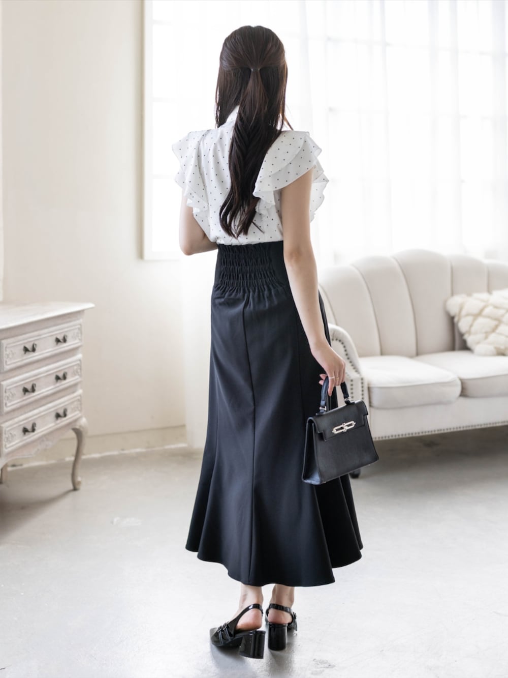 ブラック系のパンプス、ブラック系のスカート、ブラック系のハンドバッグを着用したレディースの夏コーディネートの2枚目の写真