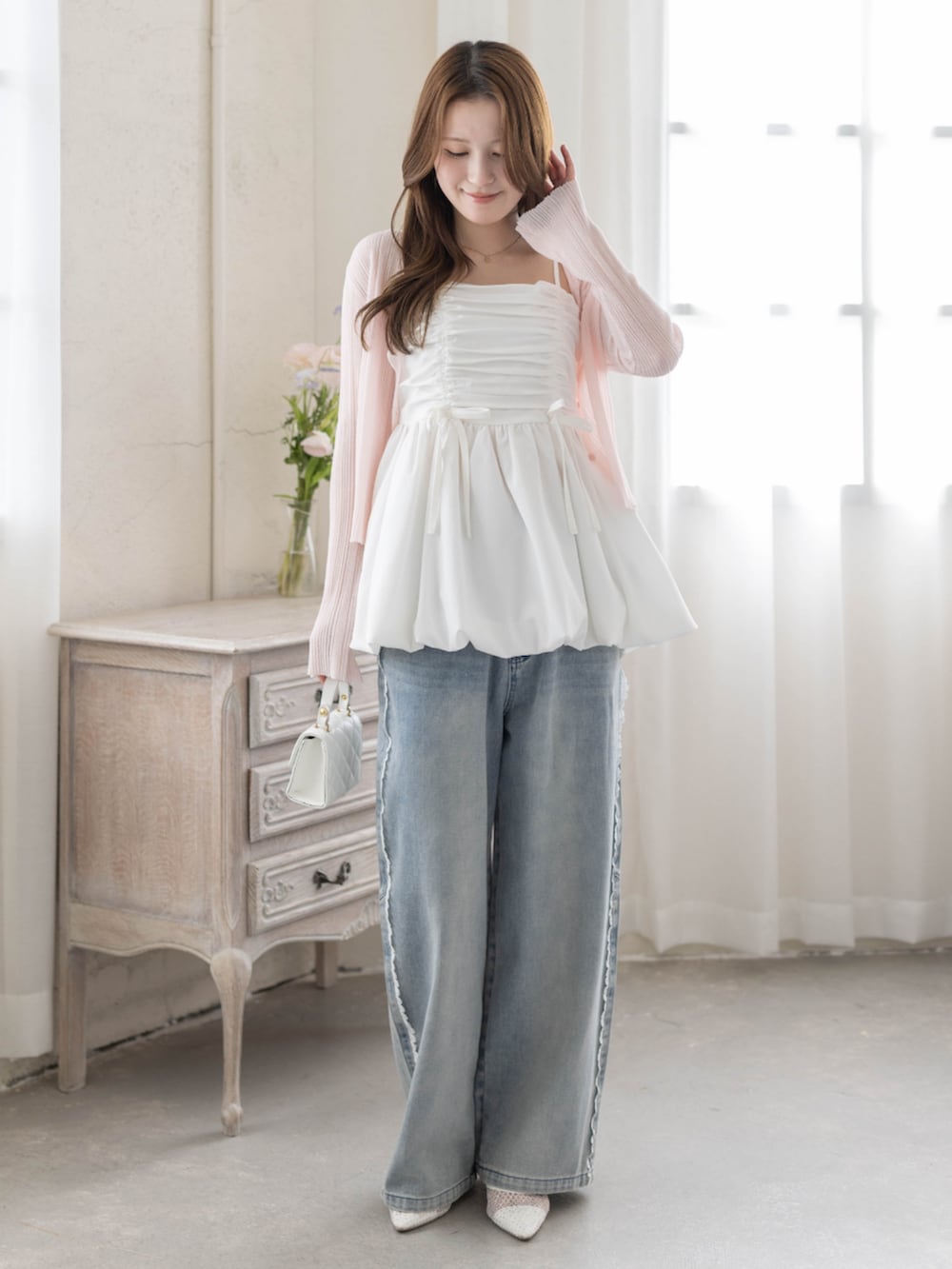 ホワイト系のチュニック、ホワイト系のパンプス、ピンク系のカーディガン/ボレロを着用したレディースの春コーディネートの2枚目の写真