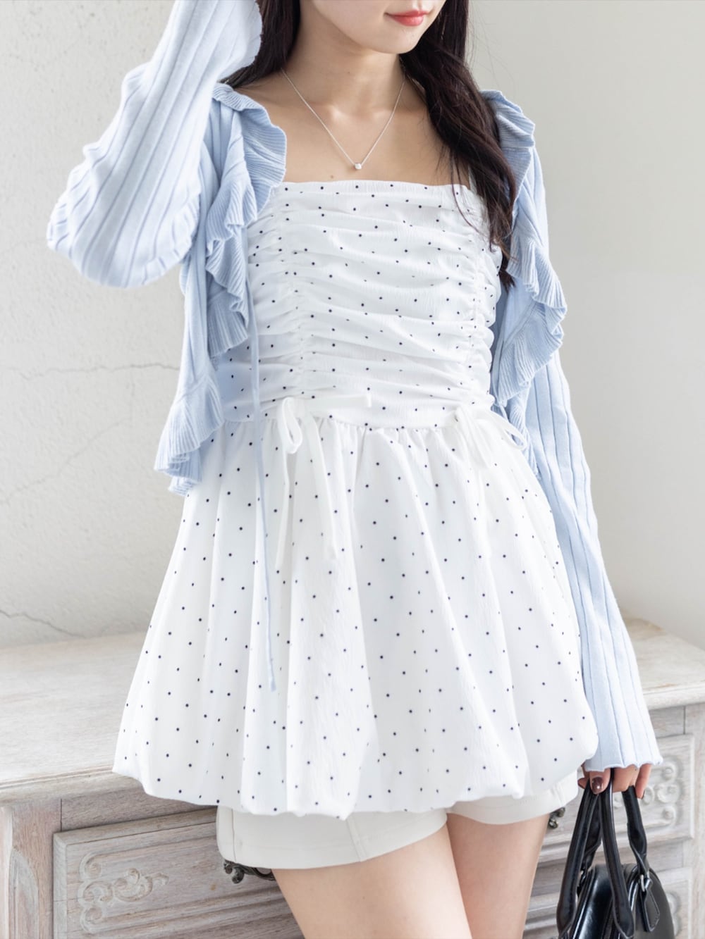 ブラック系のブーツ、ホワイト系のチュニック、ブルー系のカーディガン/ボレロを着用したレディースの春コーディネートの2枚目の写真