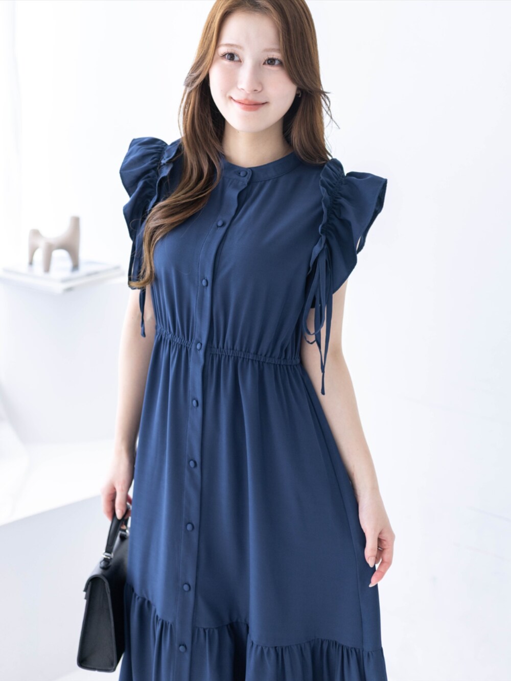 ブラック系のハンドバッグ、ブラック系のパンプス、ブルー系のワンピースを着用したレディースの春コーディネートの3枚目の写真