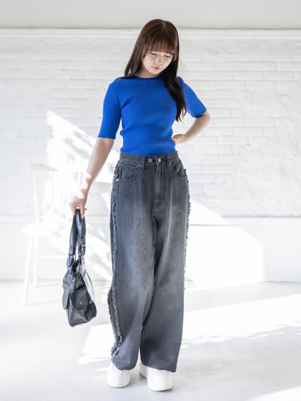 ブルー系のニット/セーター、ブラック系のハンドバッグ、ブラック系のデニムパンツを着用したレディースの春コーディネートの2枚目の写真