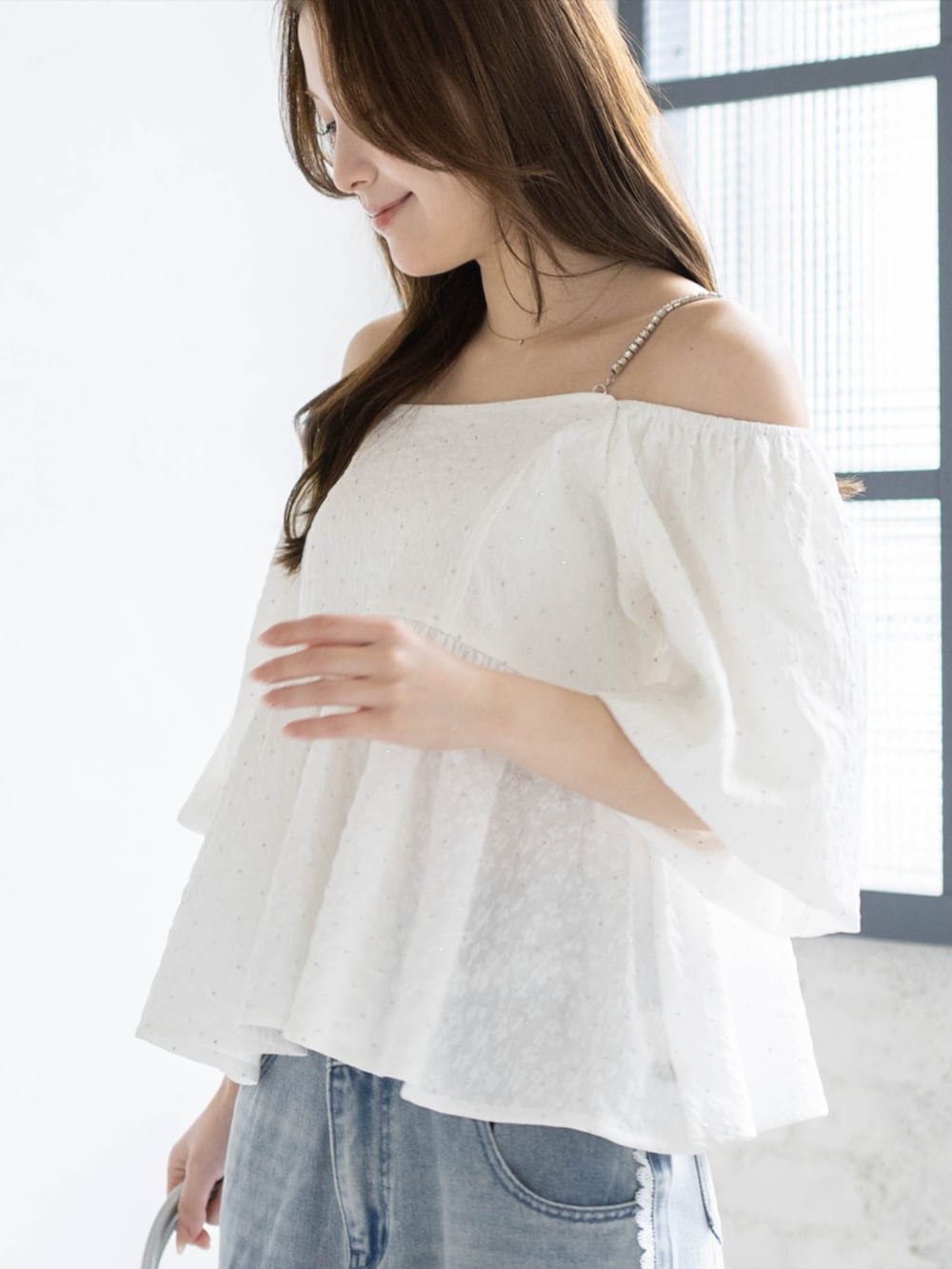 シルバー系のハンドバッグ、ブルー系のデニムパンツ、ホワイト系のパンプスを着用したレディースの春コーディネートの5枚目の写真