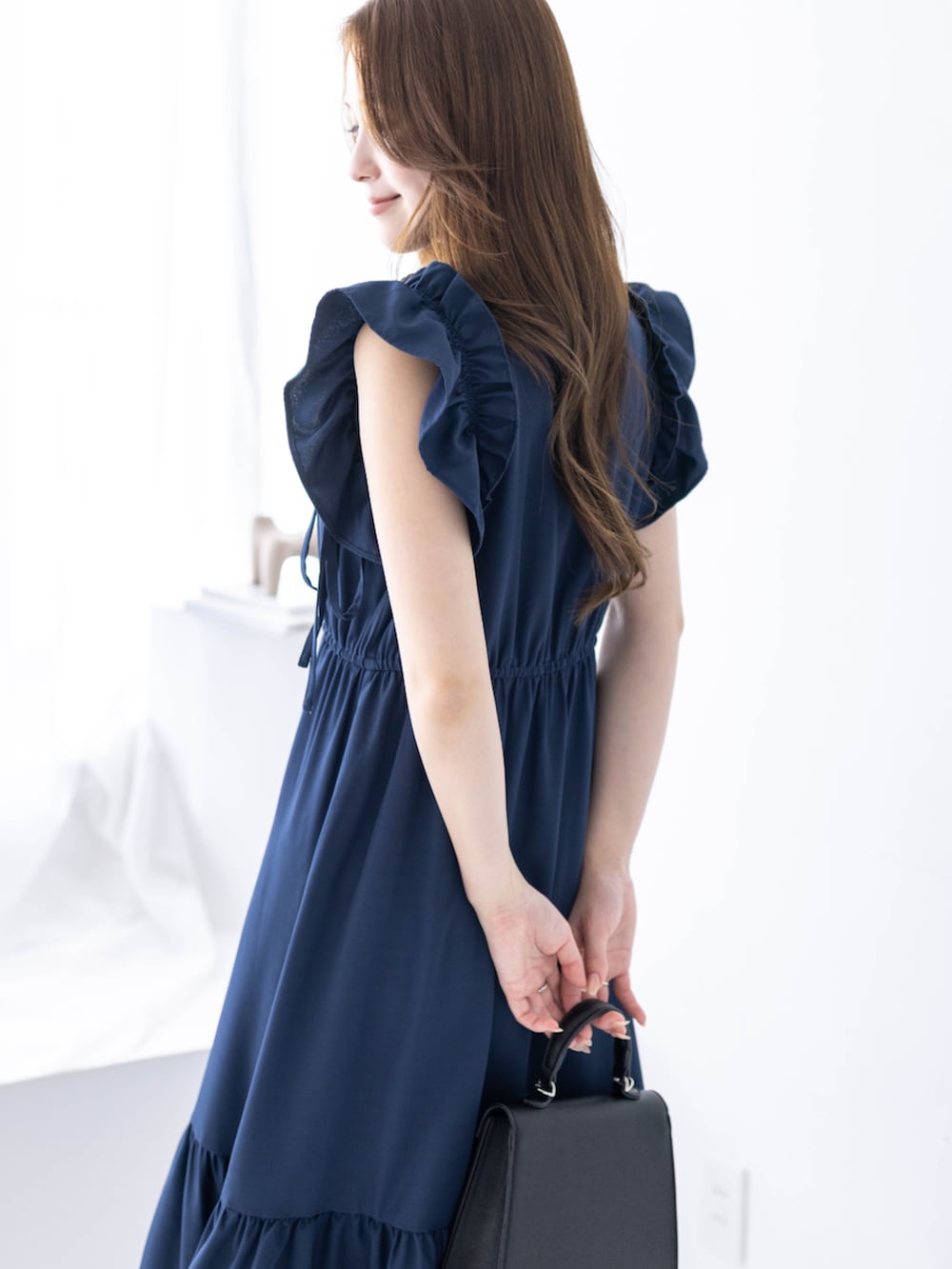 ブラック系のハンドバッグ、ブラック系のパンプス、ブルー系のワンピースを着用したレディースの春コーディネートの5枚目の写真