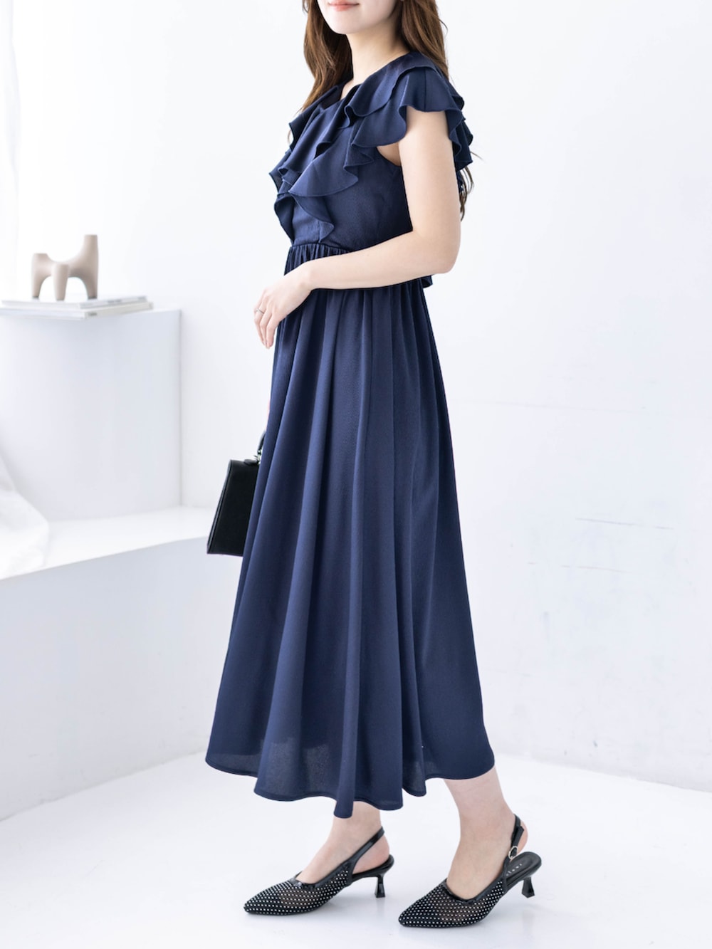 ブラック系のハンドバッグ、ブラック系のパンプス、ブルー系のワンピースを着用したレディースの春コーディネートの5枚目の写真