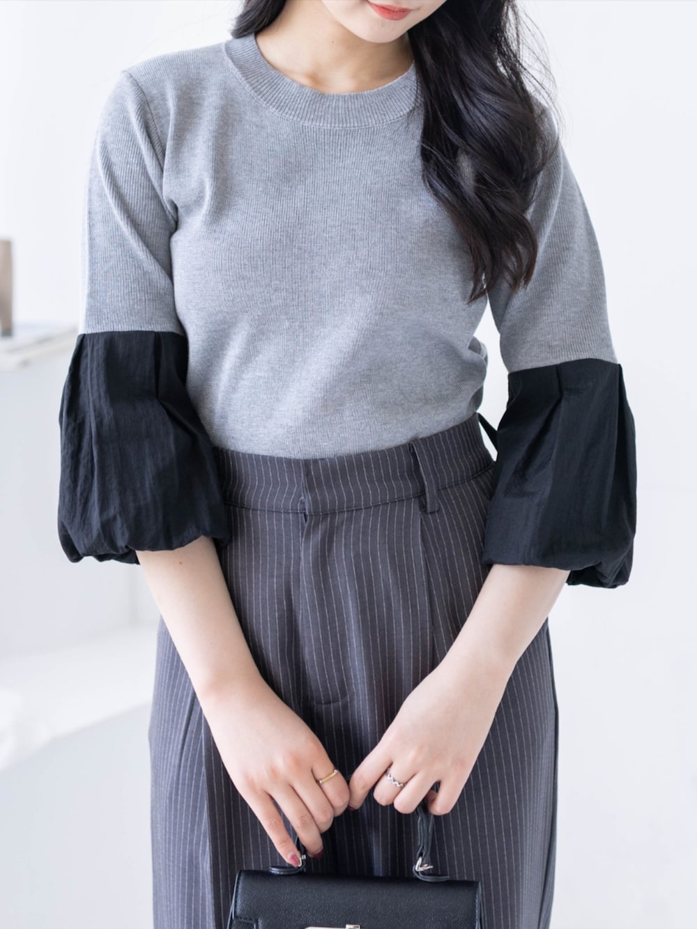 ブラック系のハンドバッグ、ブラック系のパンプス、グレー系のスラックスを着用したレディースの夏コーディネートの5枚目の写真