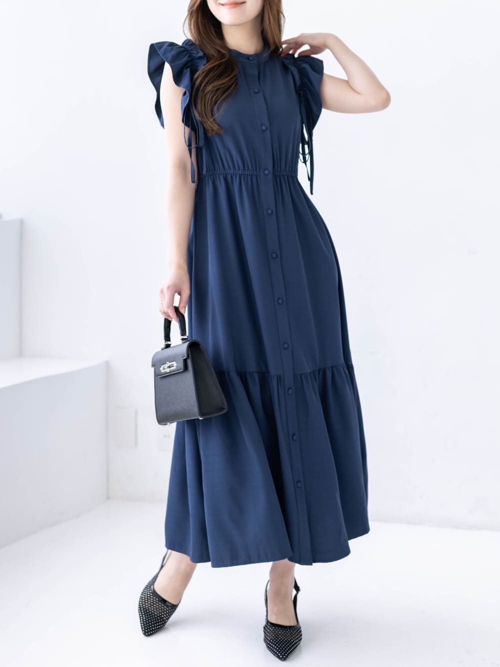 ブラック系のハンドバッグ、ブラック系のパンプス、ブルー系のワンピースを着用したレディースの春コーディネートの3枚目の写真