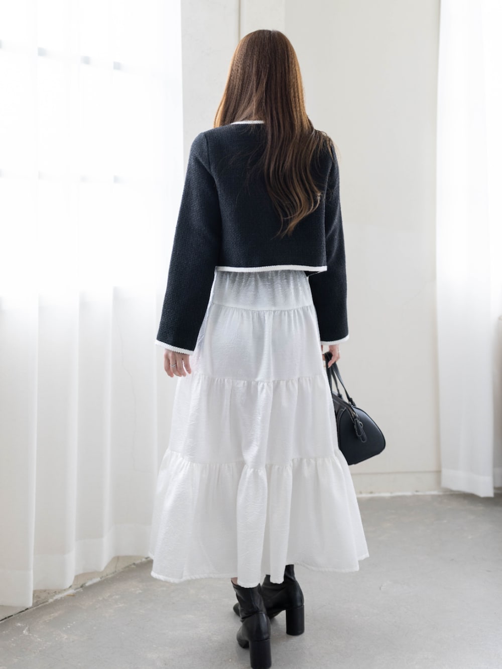 ブラック系のノーカラージャケット、ホワイト系のスカートを着用したレディースの冬コーディネートの3枚目の写真