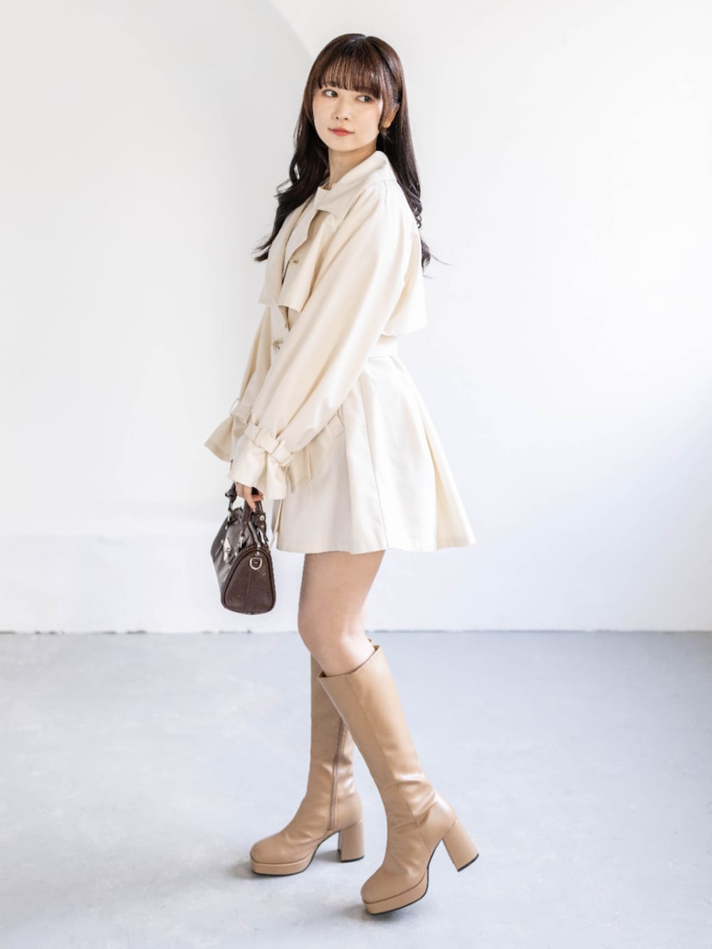 ベージュ系のブーツ、ホワイト系のトレンチコート、ホワイト系のニット/セーターを着用したレディースの春コーディネートの2枚目の写真