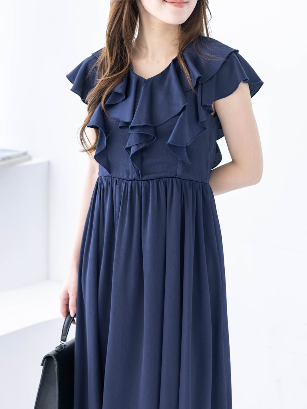 ブラック系のハンドバッグ、ブラック系のパンプス、ブルー系のワンピースを着用したレディースの春コーディネートの6枚目の写真