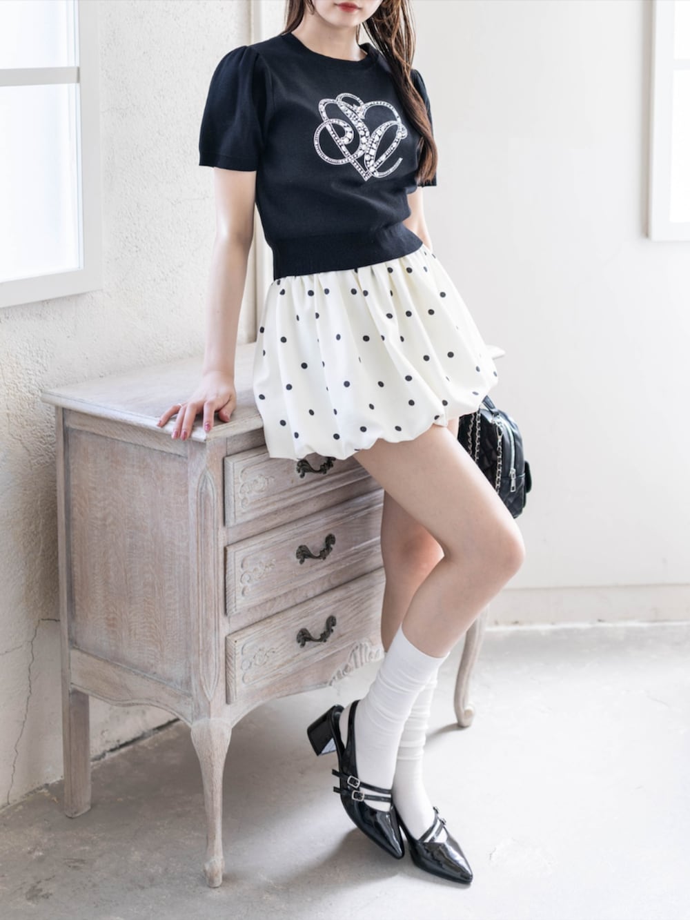 ブラック系のパンプス、ブラック系のニット/セーター、ホワイト系のスカートを着用したレディースの夏コーディネートの6枚目の写真