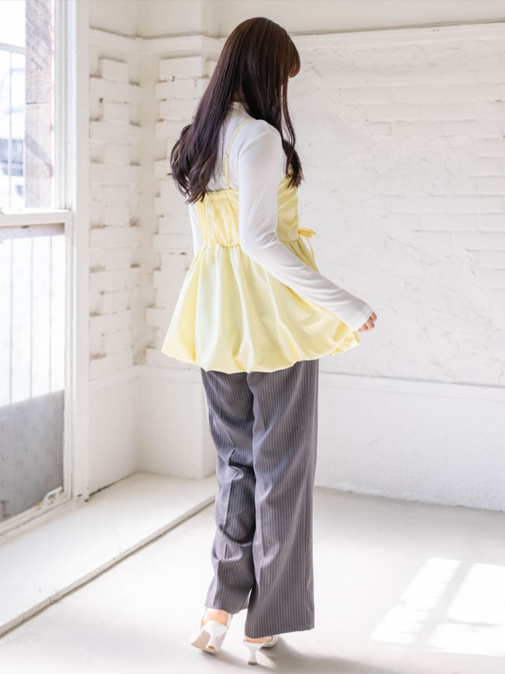 グレー系のスラックス、ホワイト系のパンプス、イエロー系のチュニックを着用したレディースの春コーディネートの3枚目の写真