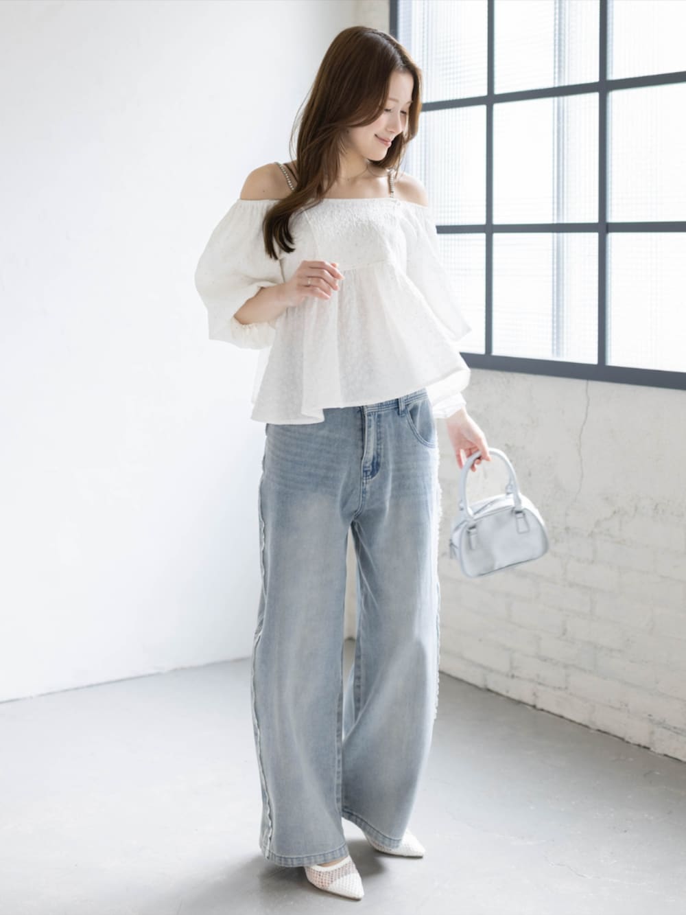 シルバー系のハンドバッグ、ブルー系のデニムパンツ、ホワイト系のパンプスを着用したレディースの春コーディネートの2枚目の写真