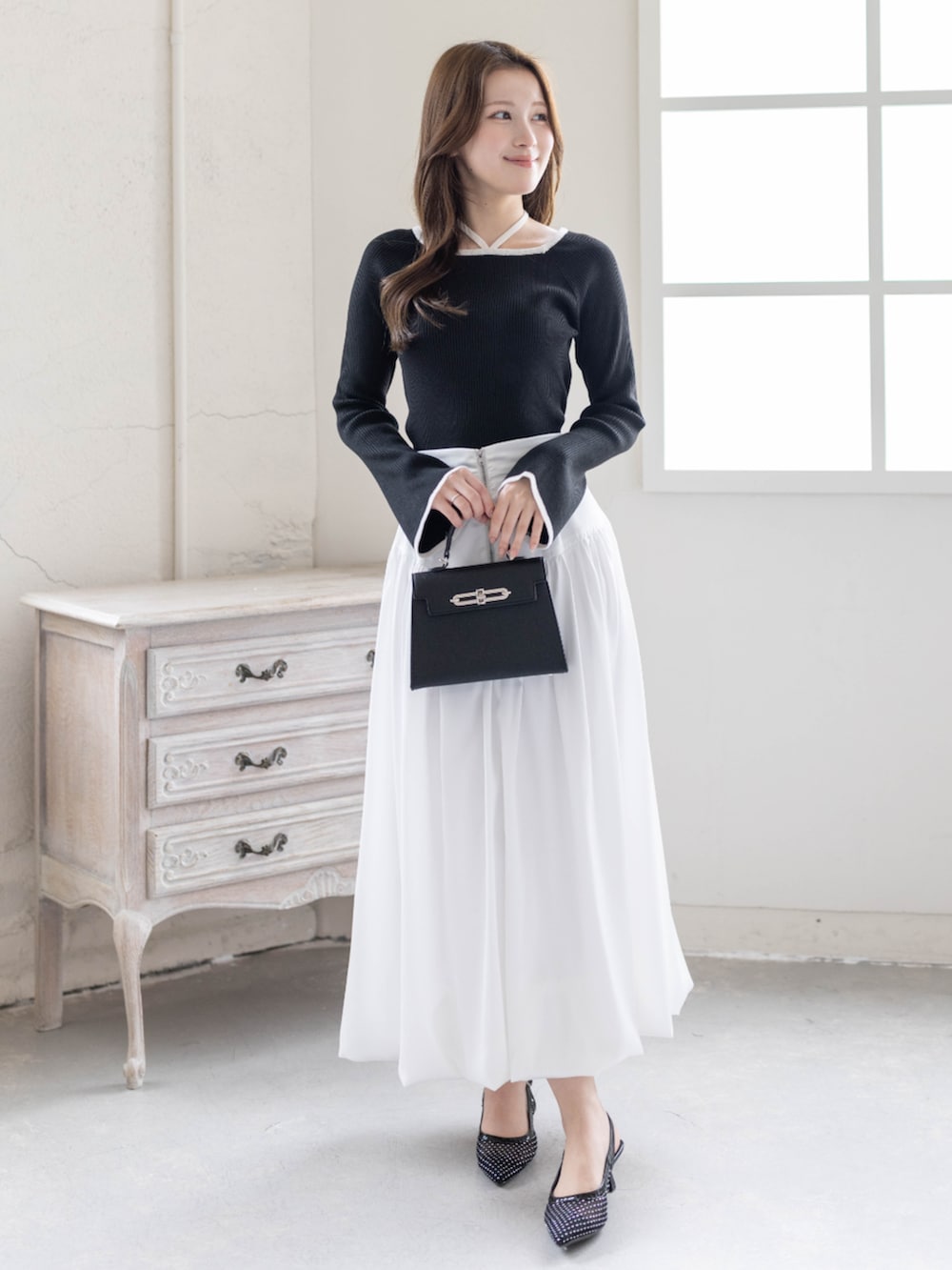 ブラック系のニット/セーター、ホワイト系のスカート、ブラック系のハンドバッグを着用したレディースの春コーディネートの2枚目の写真