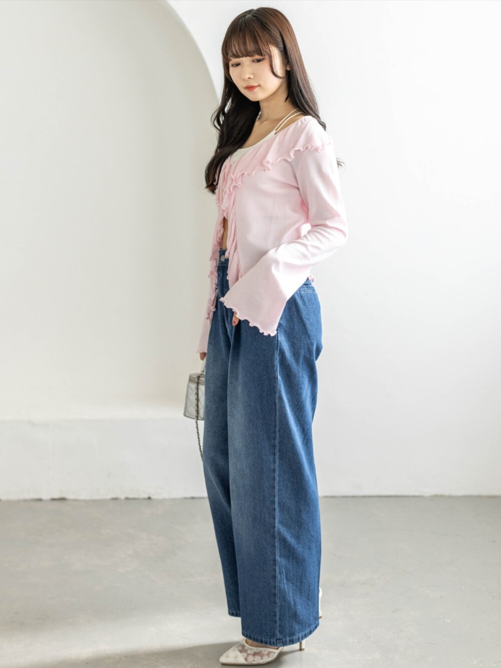 ホワイト系のパンプス、ブルー系のデニムパンツ、ピンク系のカーディガン/ボレロを着用したレディースの春コーディネートの2枚目の写真