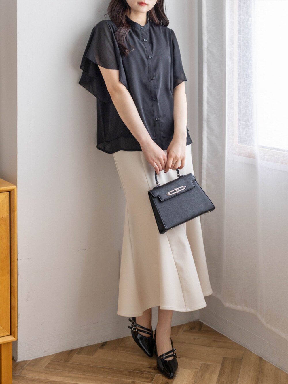 ブラック系のパンプス、ホワイト系のスカート、ブラック系のハンドバッグを着用したレディースの夏コーディネートの2枚目の写真