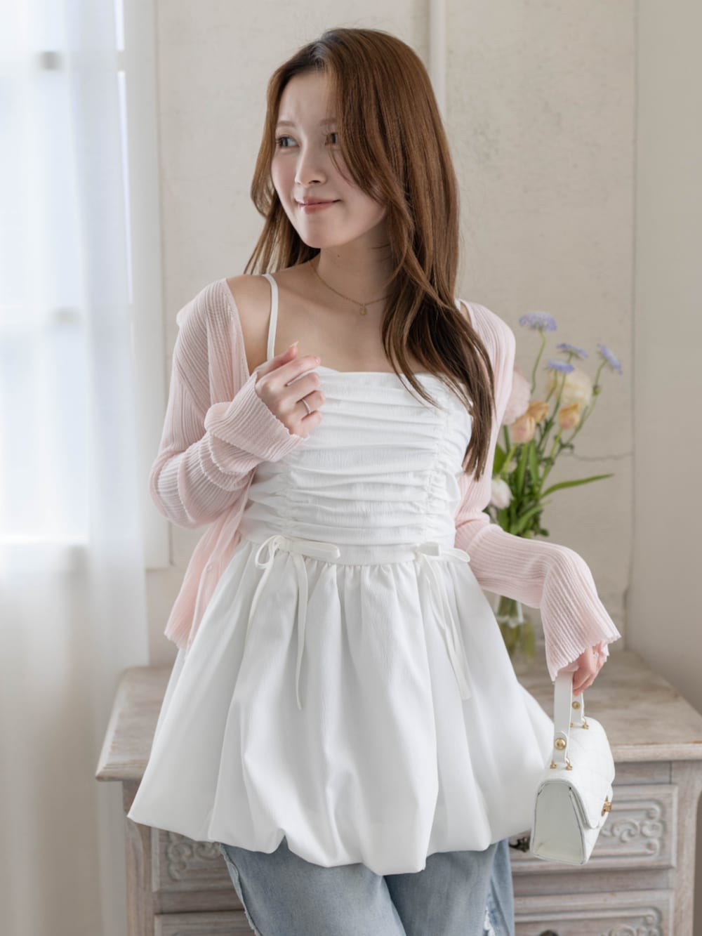 ホワイト系のチュニック、ホワイト系のパンプス、ピンク系のカーディガン/ボレロを着用したレディースの春コーディネートの4枚目の写真