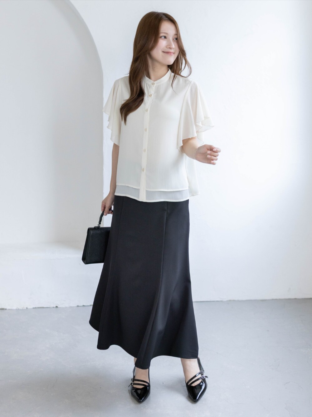 ブラック系のパンプス、ブラック系のスカート、ホワイト系のシャツ/ブラウスを着用したレディースの夏コーディネートの2枚目の写真