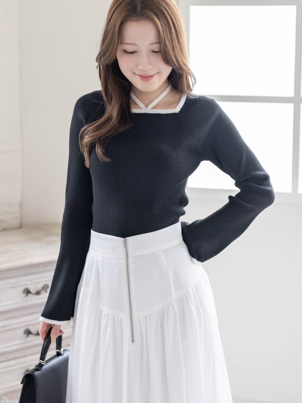 ブラック系のニット/セーター、ホワイト系のスカート、ブラック系のハンドバッグを着用したレディースの春コーディネートの3枚目の写真