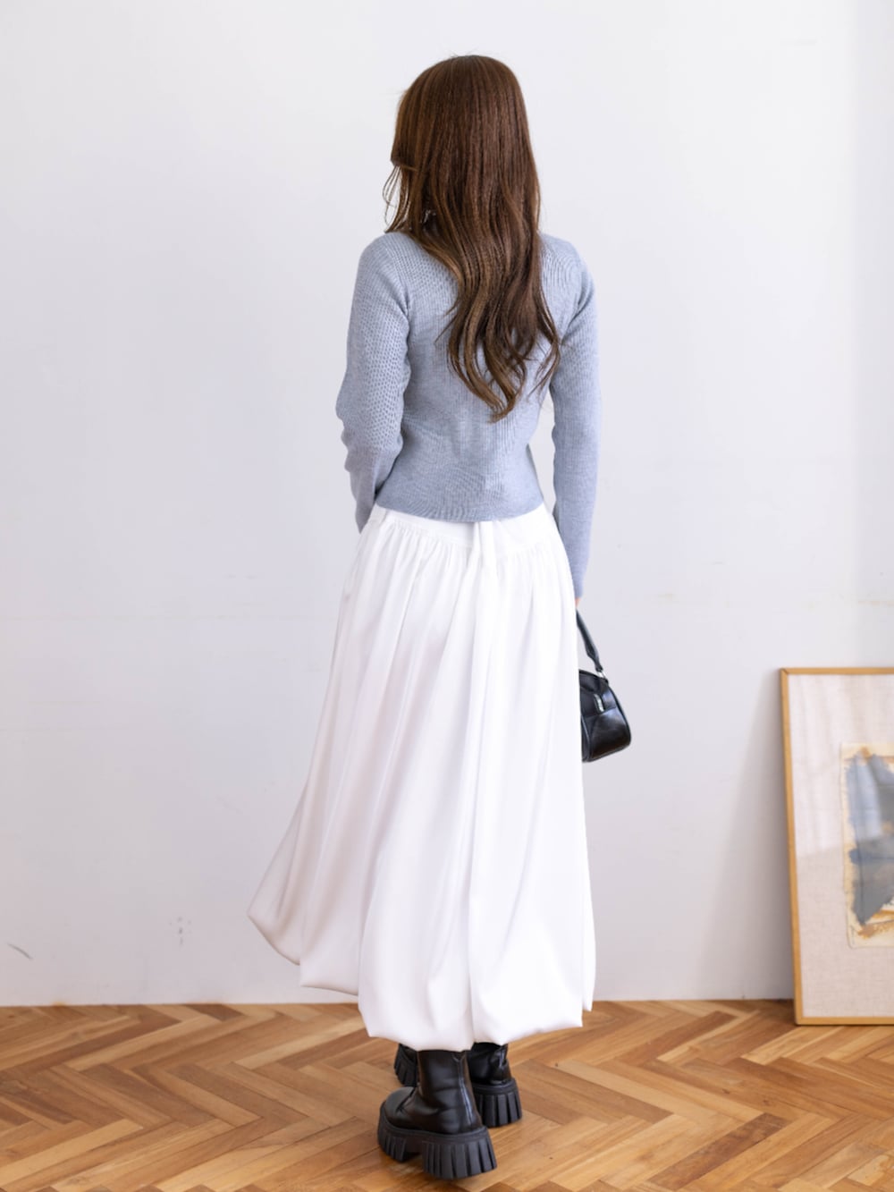 ブラック系のブーツ、グレー系のニット/セーター、ホワイト系のスカートを着用したレディースの冬コーディネートの2枚目の写真