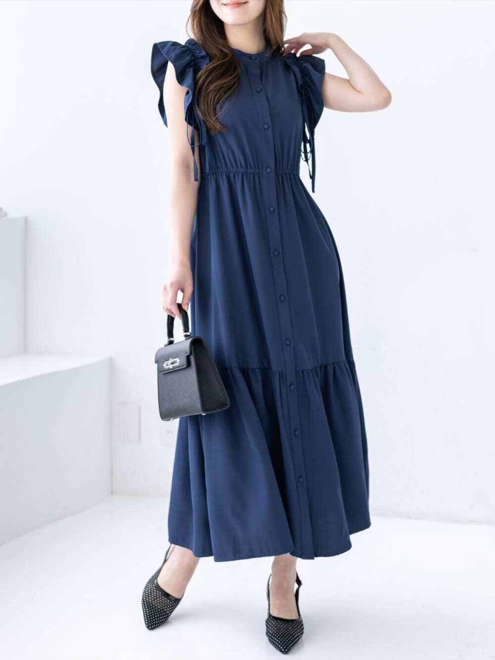 ブラック系のハンドバッグ、ブラック系のパンプス、ブルー系のワンピースを着用したレディースの春コーディネートの2枚目の写真