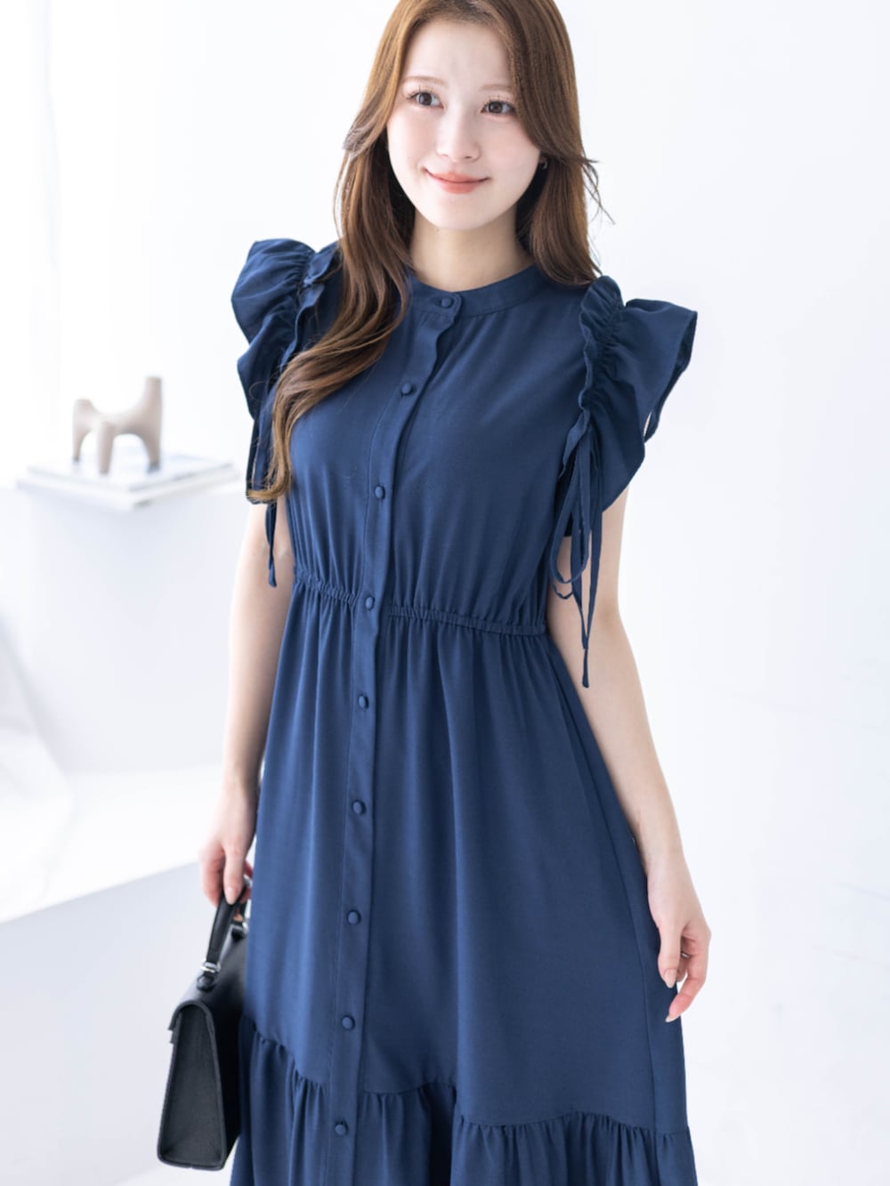 ブラック系のハンドバッグ、ブラック系のパンプス、ブルー系のワンピースを着用したレディースの春コーディネートの4枚目の写真