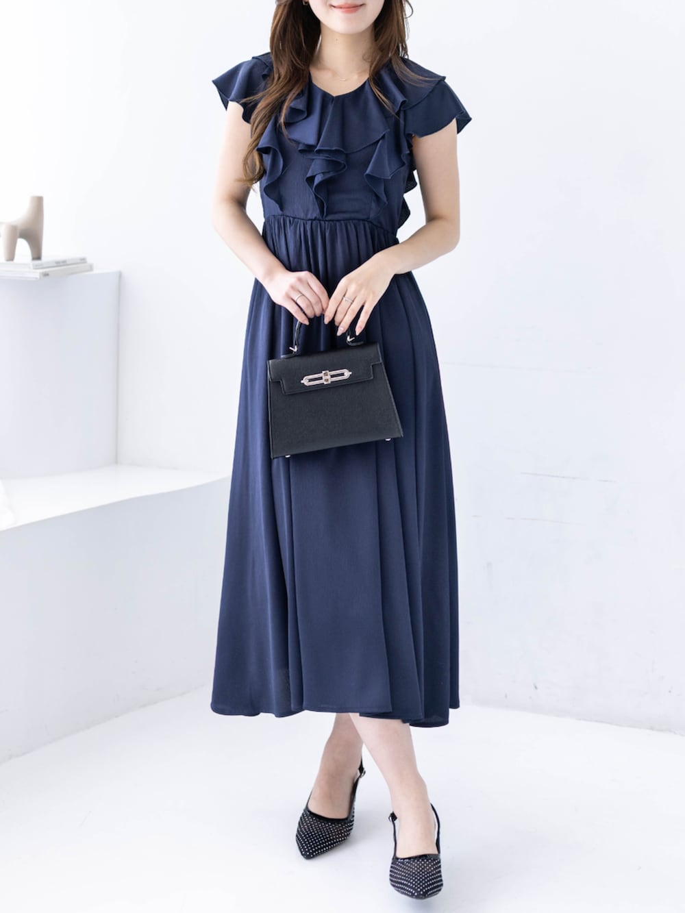 ブラック系のハンドバッグ、ブラック系のパンプス、ブルー系のワンピースを着用したレディースの春コーディネートの4枚目の写真