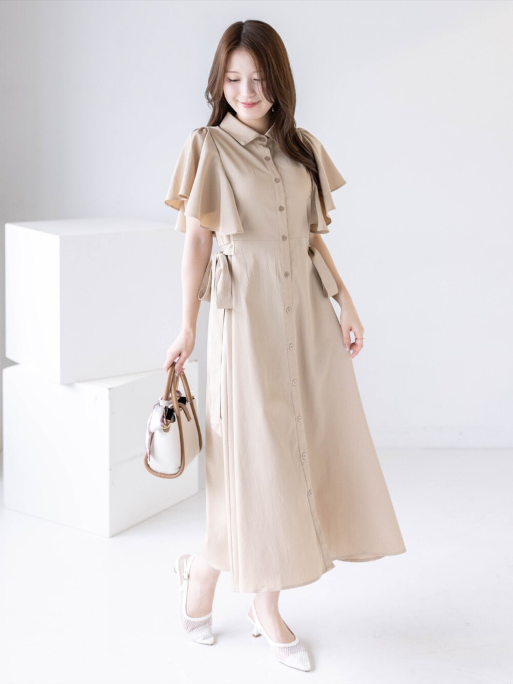 ホワイト系のパンプス、ベージュ系のワンピース、ベージュ系のハンドバッグを着用したレディースの夏コーディネートの4枚目の写真