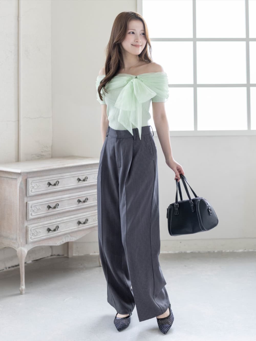 ブラック系のボストンバッグ、ブラック系のパンプス、グレー系のスラックスを着用したレディースの春コーディネートの3枚目の写真