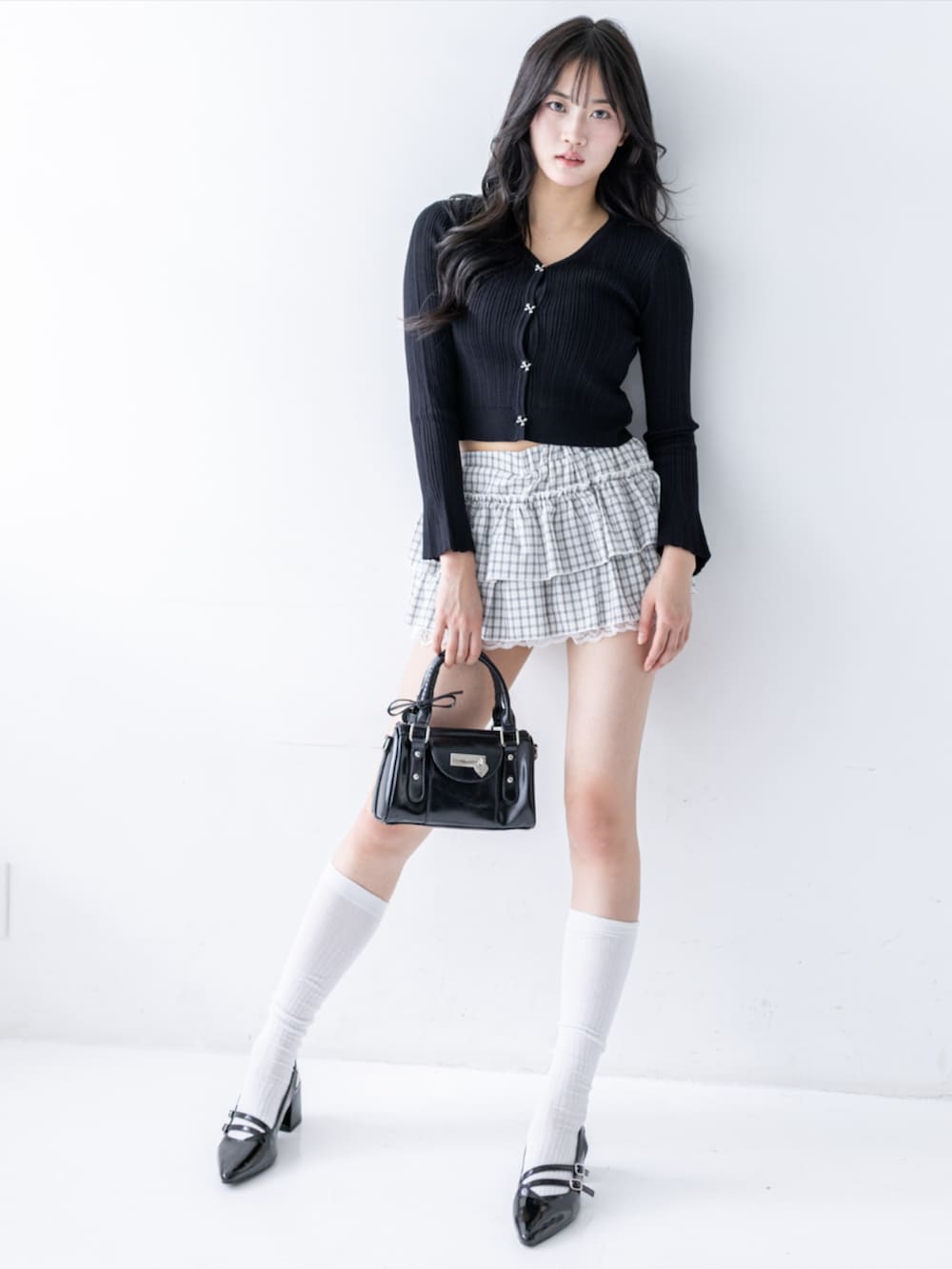ブラック系のパンプス、ブラック系のハンドバッグ、ホワイト系のスカートを着用したレディースの夏コーディネートの2枚目の写真