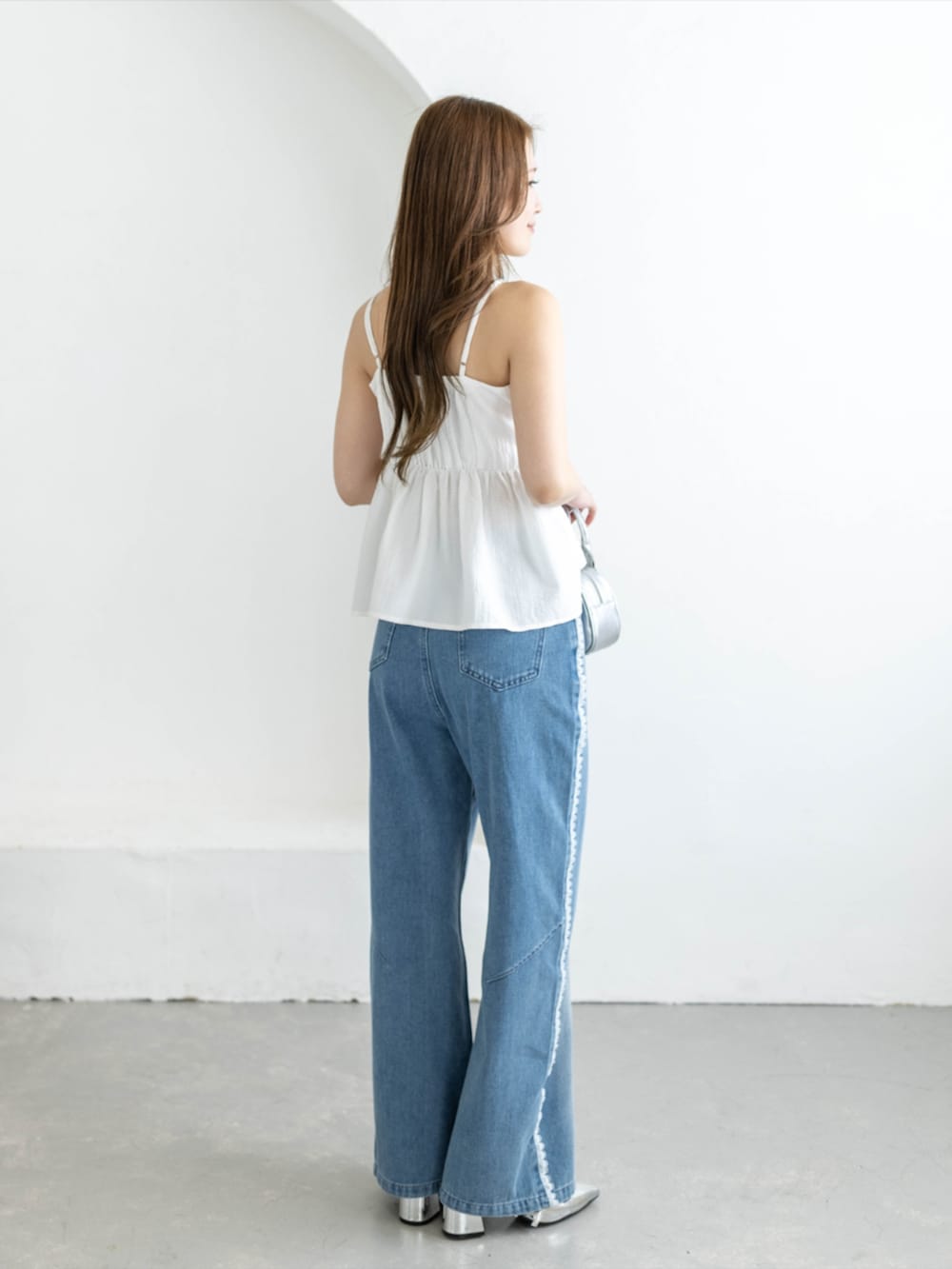 シルバー系のパンプス、ブルー系のデニムパンツ、ホワイト系のキャミソールを着用したレディースの夏コーディネートの3枚目の写真