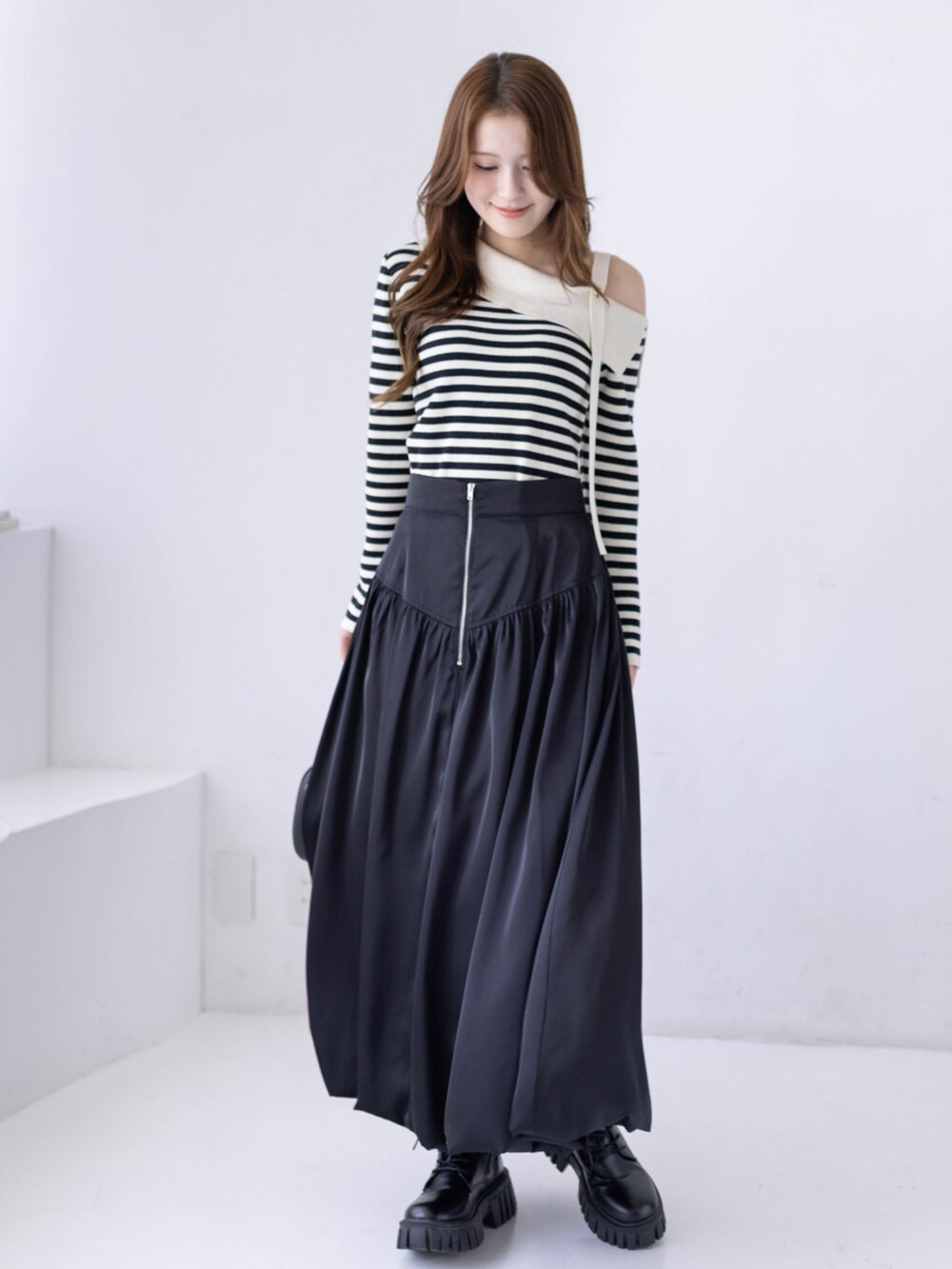 ブラック系のブーツ、ホワイト系のニット/セーター、ブラック系のスカートを着用したレディースの冬コーディネートの2枚目の写真