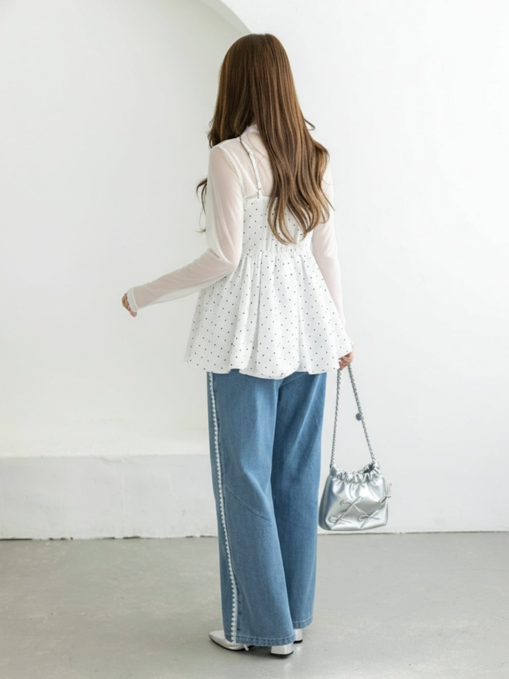 シルバー系のパンプス、ホワイト系のチュニック、ブルー系のデニムパンツを着用したレディースの冬コーディネートの2枚目の写真